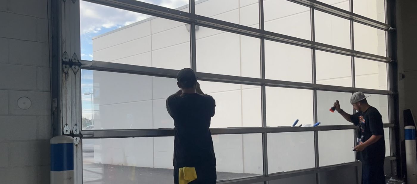 Two technicians installing window film across a large commercial storefront glass bay