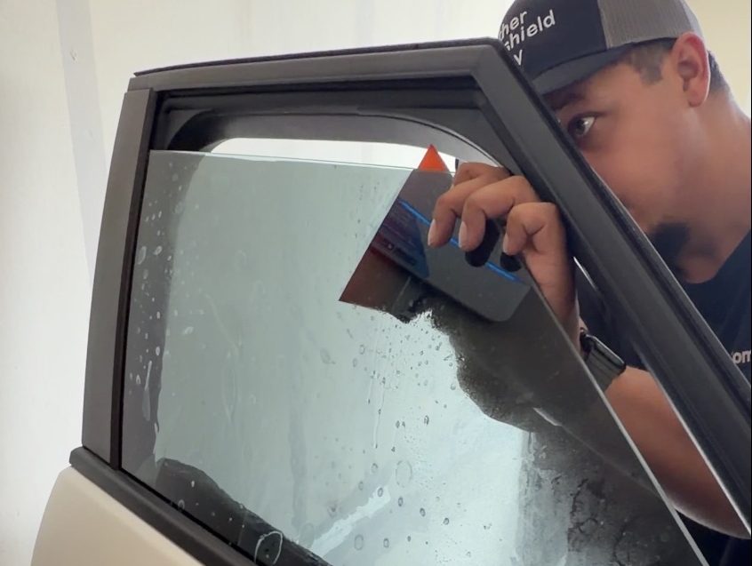 Technician squeegeeing window film onto a car door window
